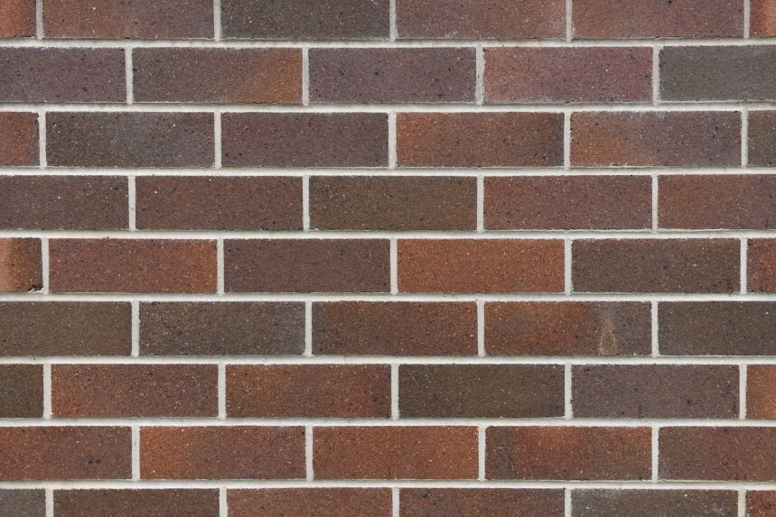 A close-up view of a brick wall highlights the Architectural Federation Red Blend, featuring a mix of brown and red hues arranged in horizontal rows. The bricks display subtle tonal variations, achieving a consistent yet textured look, while the light gray mortar complements this striking design.