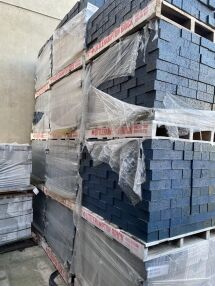 Laguna Glazed Bricks, stacked on wooden pallets, wrapped in clear plastic, and labeled Littlehampton Brick, are stored outdoors against a beige wall.