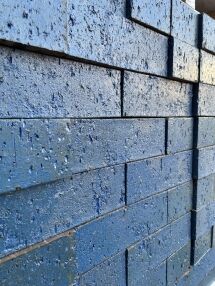 A close-up of blue Laguna Glazed Bricks shows visible texture and minor wear on each brick surface, with the bricks arranged in horizontal rows.
