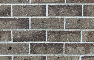 Close-up of a brown brick wall showcasing a pattern of horizontal and vertical mortar lines in architectural detail. The bricks, featuring their rough texture and varied shades, subtly enhance the dark silver grey shadows from the Architectural Dark Silver Grey product, highlighted by small spots and imperfections on the surface.
