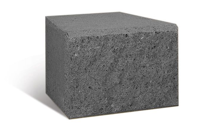 A New Miniwall Charcoal concrete block, featuring a solid structure, rough texture, and straight edges in a rich charcoal color rests on a white surface. The shadows cast on its left side and below suggest the light source is positioned to its right.