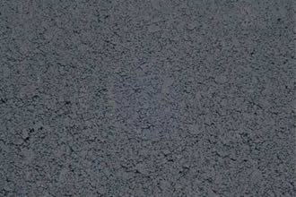 Close-up of a dark gray surface, identified as Broadway Charcoal. The texture appears granular and uneven, similar to asphalt or compacted soil.