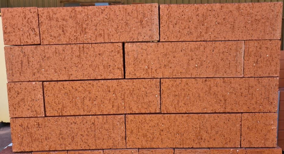 A collection of Modular Terracotta Wirecut bricks arranged in three uneven rows against a neutral background. The bricks exhibit a slightly speckled texture and are positioned in a loose, staggered pattern.